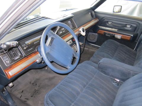 1991 Ford LTD Crown Victoria - The interior of a 1991 Ford Crown Victoria LTD features blue velour seats, wood grain trim, and a dashboard with a prominent speedometer.