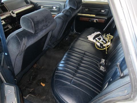 1991 Ford LTD Crown Victoria - Rear interior of a car with dark seats and floor mats, a white shirt and gold chain are on the back seat.