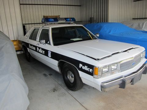 1991 Ford LTD Crown Victoria - A white police car with a black stripe and 'Boston Police' text is parked inside a garage.
