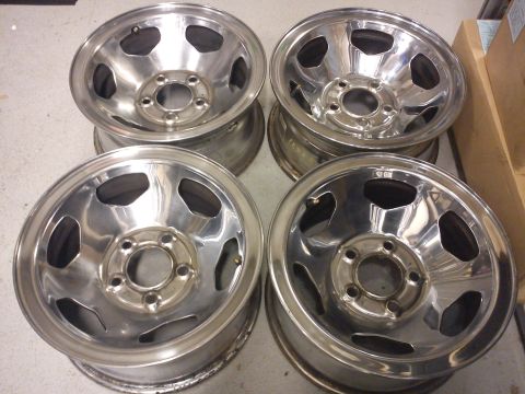 1997 Chevrolet Silverado 1500 - A set of four chrome wheels, each with a five-lug pattern and a five-spoke design, are displayed on a concrete surface.