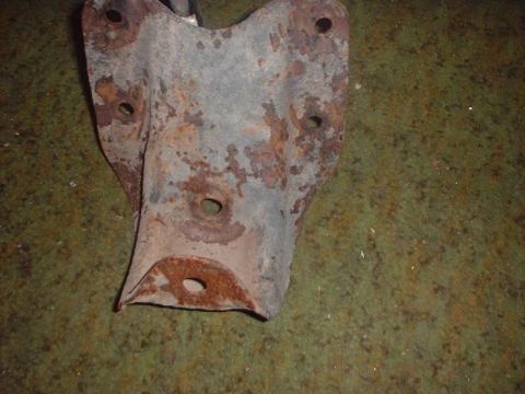 1993 Ford Bronco - A heavily rusted metal bracket with several holes is shown against a textured green background.