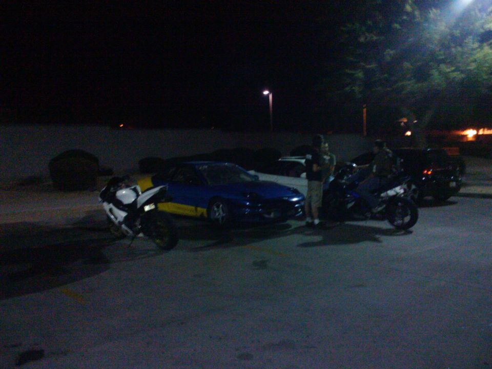 Blue and yellow 1993 Ford Probe parked with motorcycles at night
