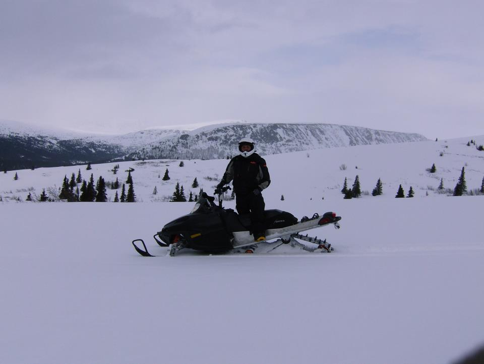 Person on a snowmobile in a snowy landscape with mountains in the background