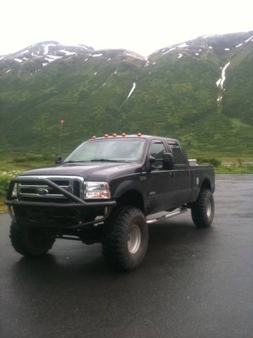 1990 Chevrolet Suburban - A black pickup truck is parked on a wet road with a mountainous landscape behind it.