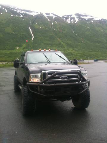 1990 Chevrolet Suburban - This black Ford F-Series truck features a heavy-duty custom bumper and oversized tires, parked in front of a mountain landscape.