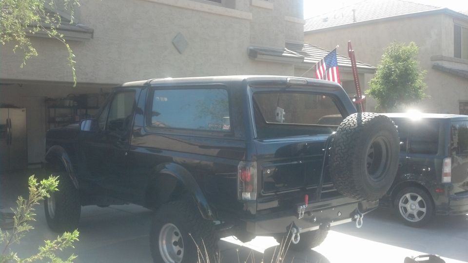 Black SUV, 1992 Ford Bronco, parked in driveway, rear view, spare tire mounted on swing away carrier
