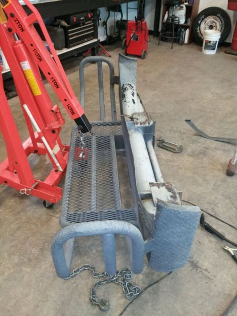 1995 Ford F-150 - A detached truck bumper sits on a shop floor next to a red engine hoist.