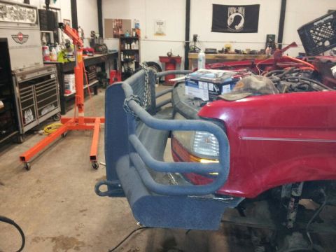 1995 Ford F-150 - Front view of a red truck a custom bumper and exposed engine parts, likely undergoing repairs or modifications.