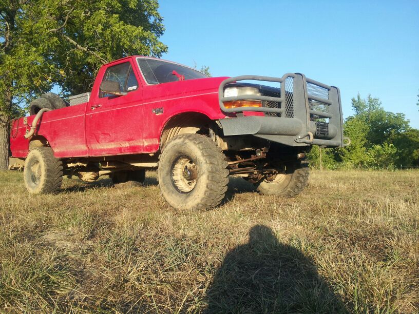 Red 1995 Ford F-150 pickup truck with a large bull bar on the front, parked in a grassy field