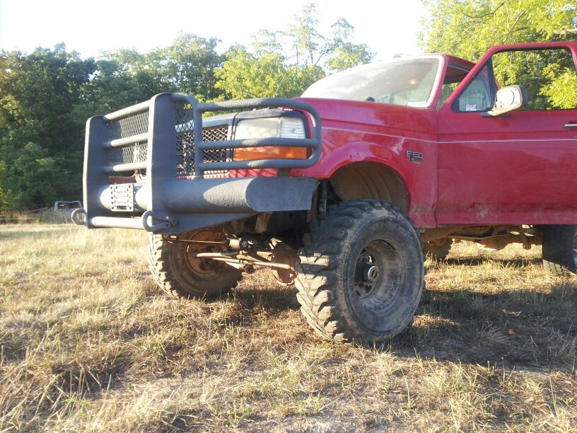 Red Ford F-250 truck with a large brush guard and off-road tires, parked in a grassy field