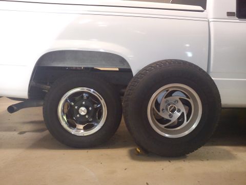 1997 Chevrolet Silverado 1500 - A white pickup truck's rear wheel well is shown with two different wheels and tires placed beside it.