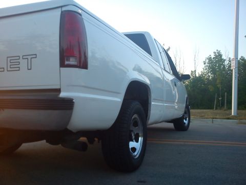 1997 Chevrolet Silverado 1500 - A white pickup truck is parked on a street with trees and a pole in the background.