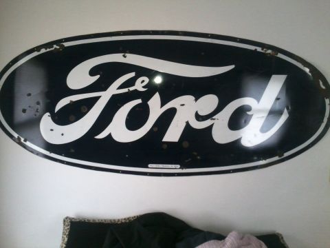 1966 Ford Bronco - Large oval Ford script logo sign in black and white porcelain enamel with chipped edges, mounted on an interior wall.
