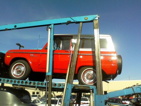 1966 Ford Bronco - A red and white Ford Bronco is transported on a car carrier.