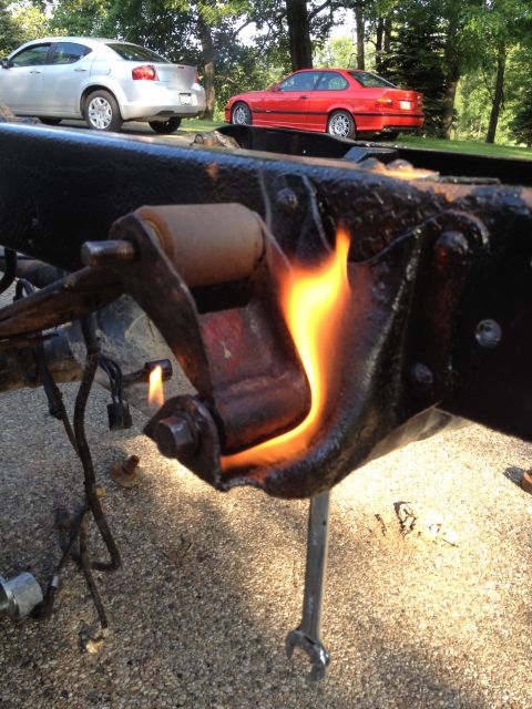 1986 Ford Bronco - A vehicle frame component is heated by a torch, with two cars visible in the background.