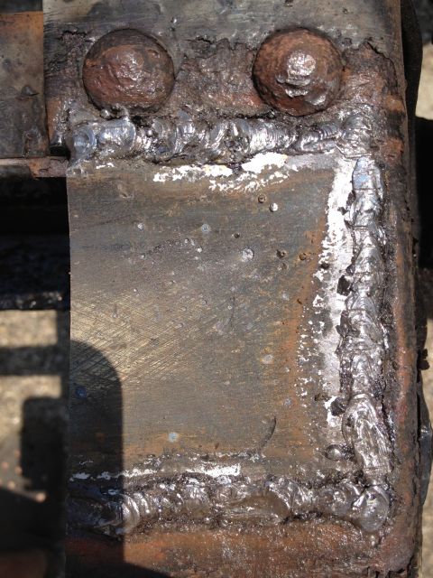 1986 Ford Bronco - This image shows a section of a heavily rusted metal frame with crude welds and large bolts, indicating repair work.