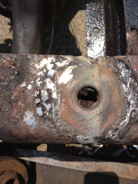 1986 Ford Bronco - This image shows a heavily rusted metal frame component with a central hole and visible welding, suggesting it is a part undergoing repair…