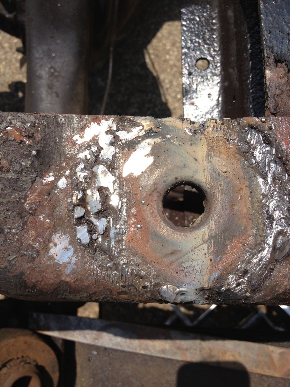 Close-up of rusted metal frame with a hole and welding marks