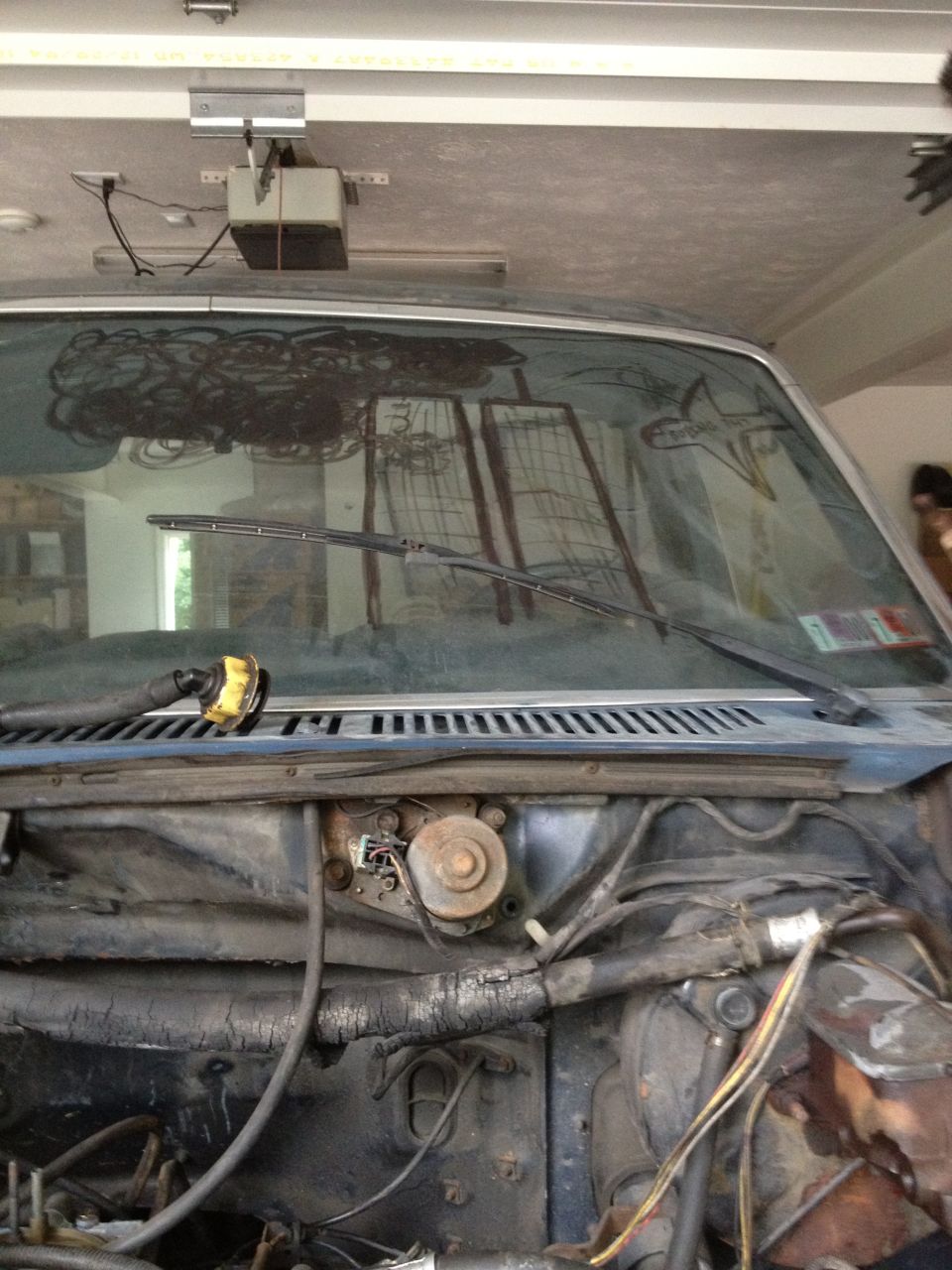Vehicle windshield with wiper blades and reflection, showing engine bay components below