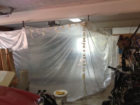 1986 Ford Bronco - A vehicle is covered in plastic sheeting, likely for a paint or repair project, within a garage setting.