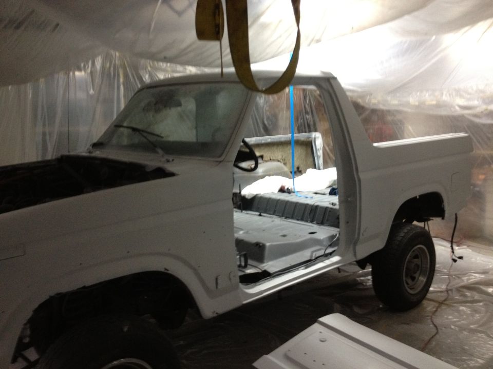White Ford Bronco in a paint booth, doors open, interior stripped, hood up