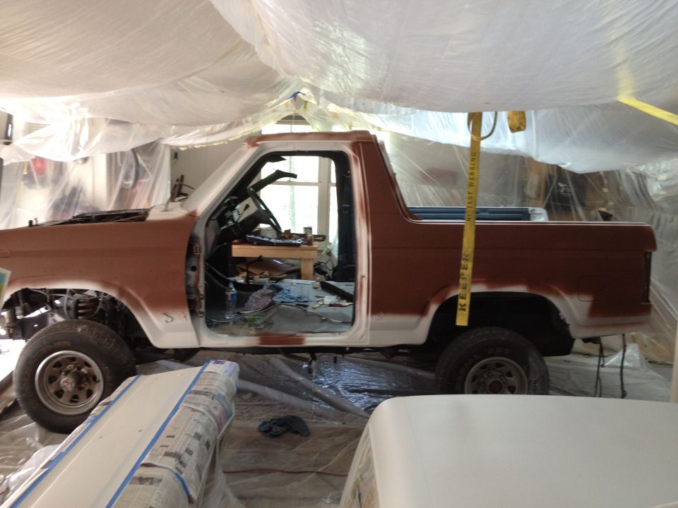 Brown and white Ford Bronco in side view, undergoing restoration with doors open and hood up