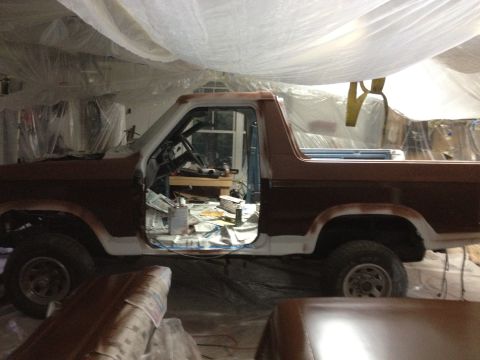 1986 Ford Bronco - A Ford Bronco is seen in a garage with its door open, covered in plastic sheeting and undergoing repairs.