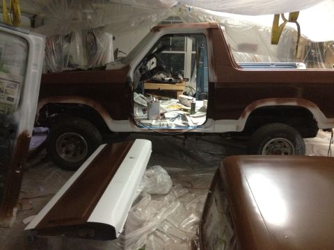 1986 Ford Bronco - A Ford Bronco is being worked on in a garage, with parts removed and paint supplies visible.
