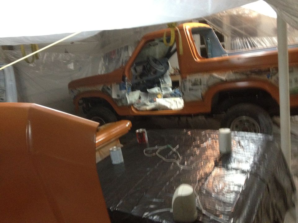Orange 1986 Ford Bronco with doors open, undergoing paintwork