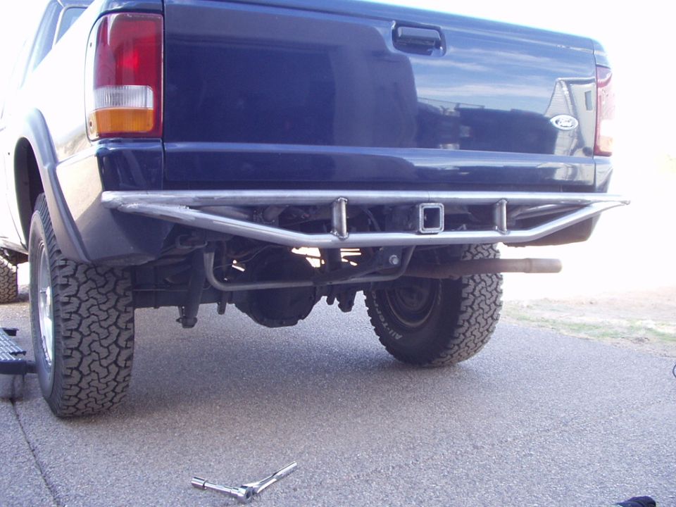 Dark blue Ford rear with custom tubular metal bumper and hitch, on a concrete drive