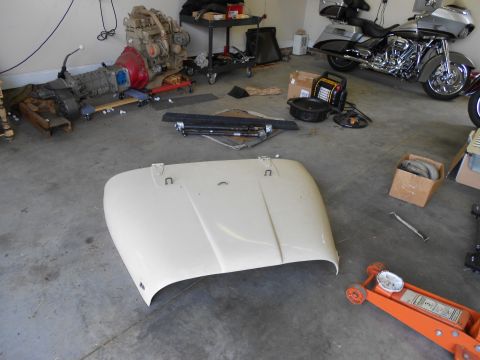 1986 Jeep Wagoneer - A detached beige Jeep hood rests on the floor of a garage, surrounded by various automotive parts and a motorcycle.