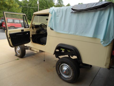 1986 Jeep Wagoneer - A tan Jeep CJ-8 Scrambler is parked outside with its driver's door open and a tarp covering the rear bed area.
