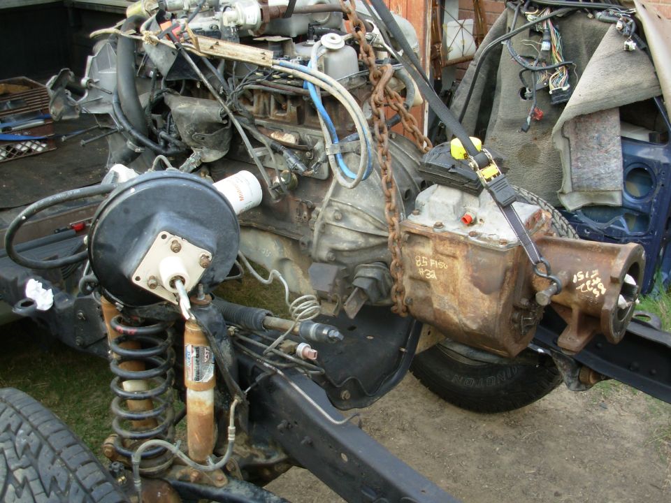Truck engine and transmission on frame, chain-supported, marked '85 F150', outdoors