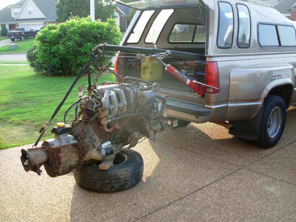 Engine and transmission hoisted from bed of tan dually pickup in driveway