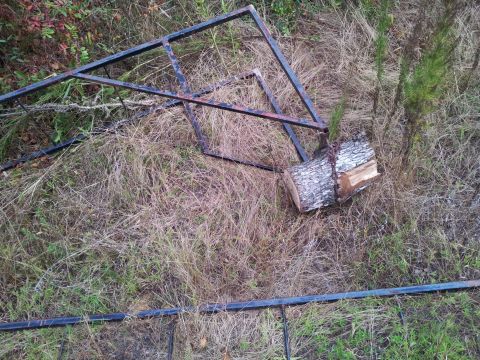1986 Ford Bronco - A metal frame and a log lie on the ground amidst dry grass and foliage.