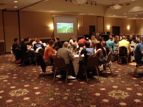 1992 Ford Taurus - A gathering of people seated at tables in a room, with a projector screen showing an image in the background.