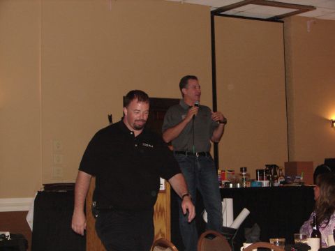 1992 Ford Taurus - A man speaks into a microphone while another man walks past him on a stage during an event.