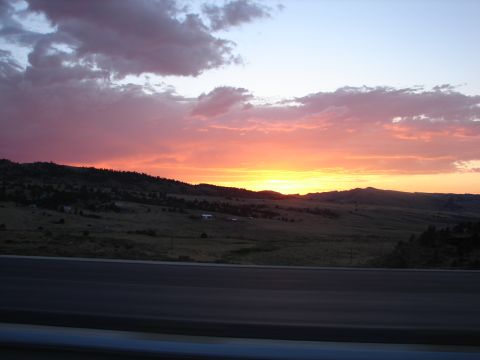 1992 Ford Taurus - A vibrant sunset paints the sky over a rural landscape, with a highway visible in the foreground.