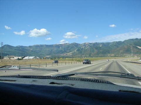 1992 Ford Taurus - View from inside a vehicle driving on a highway with mountains in the distance under a blue sky with clouds.