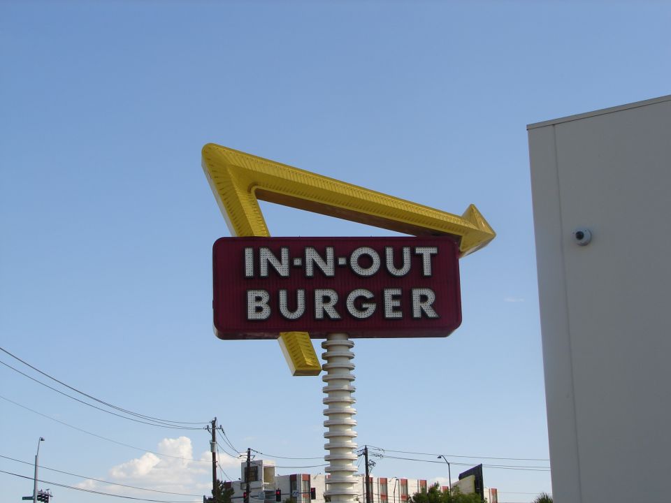 In-N-Out Burger sign against a blue sky with a white building to the right
