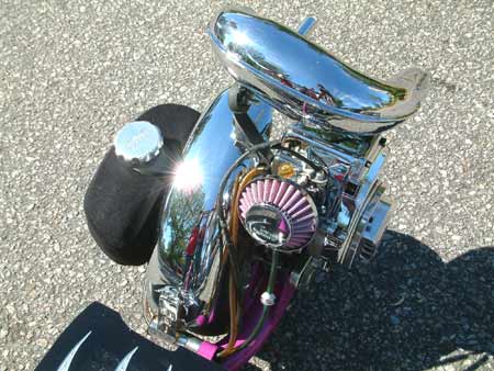 1990 Ford Bronco - Close-up of a custom chrome engine assembly a pink air filter and a black fuel tank, set against an asphalt background.