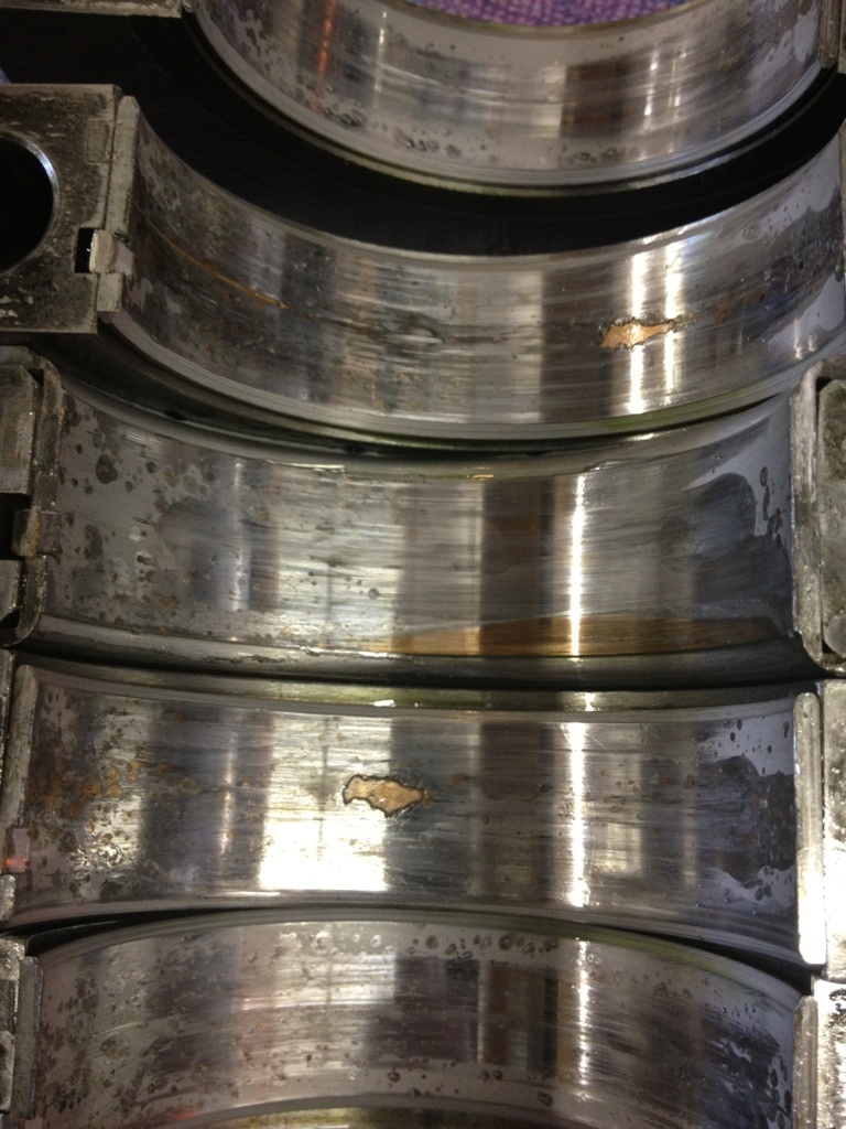 Engine bearings with visible wear and damage, showing scoring and pitting
