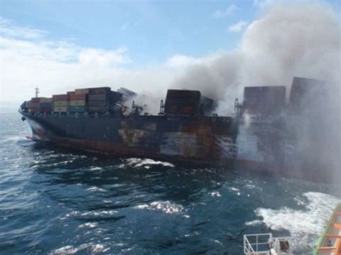 1991 Ford LTD Crown Victoria - A large cargo ship is engulfed in flames and smoke while at sea.