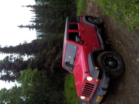 1990 Chevrolet Suburban - A red Jeep Wrangler navigates a muddy trail surrounded by dense forest.