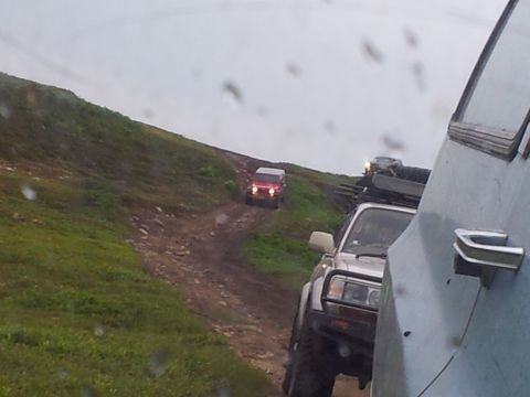 1990 Chevrolet Suburban - Multiple off-road vehicles navigate a challenging dirt track on a cloudy day.