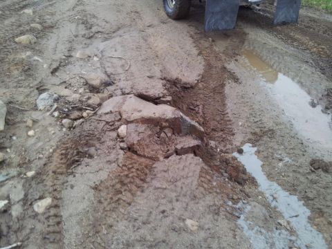 1990 Chevrolet Suburban - The rear of a dark SUV is visible on a muddy, rutted road with several puddles.