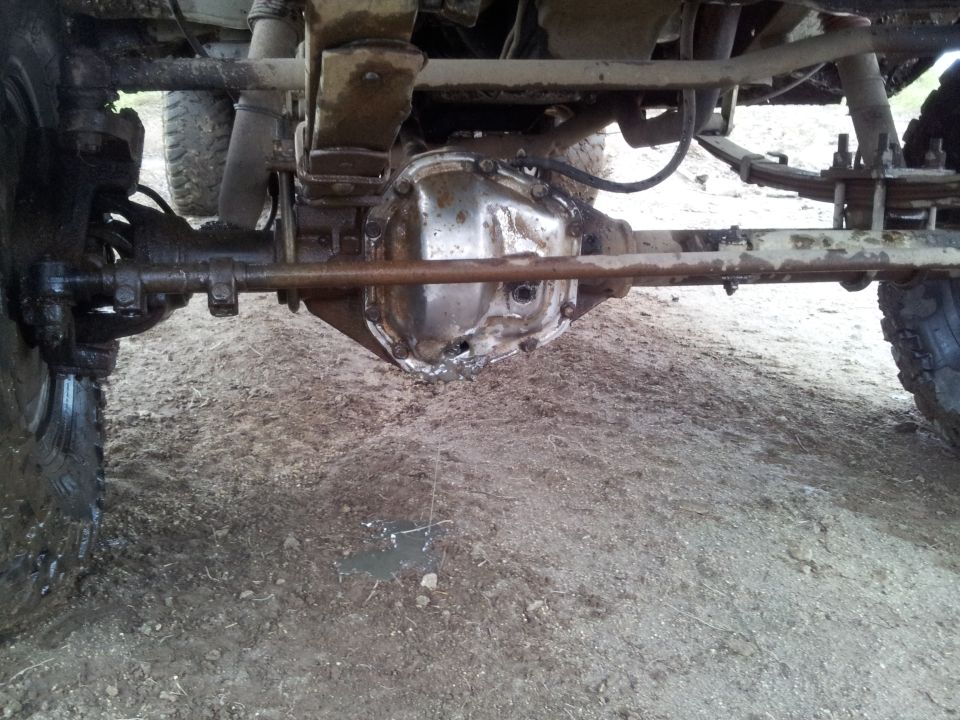 Underside view of a vehicle's rear differential and leaf spring suspension. The differential cover appears damaged