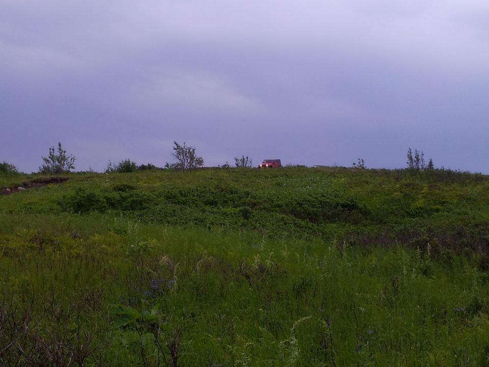 Red SUV parked on a hill under a cloudy sky