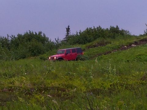 1990 Chevrolet Suburban - Red Jeep Wrangler Unlimited navigates a grassy, off-road path under an overcast sky.