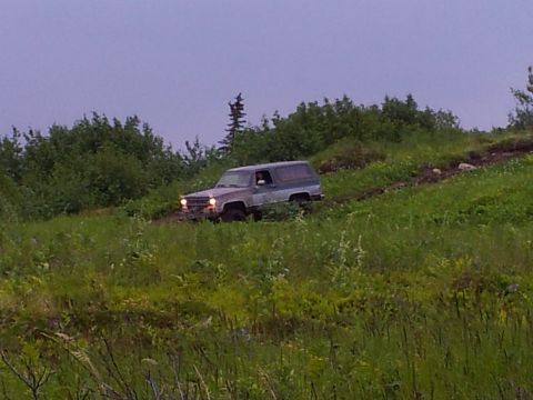 1990 Chevrolet Suburban - A two-tone SUV navigates a grassy incline under an overcast sky.